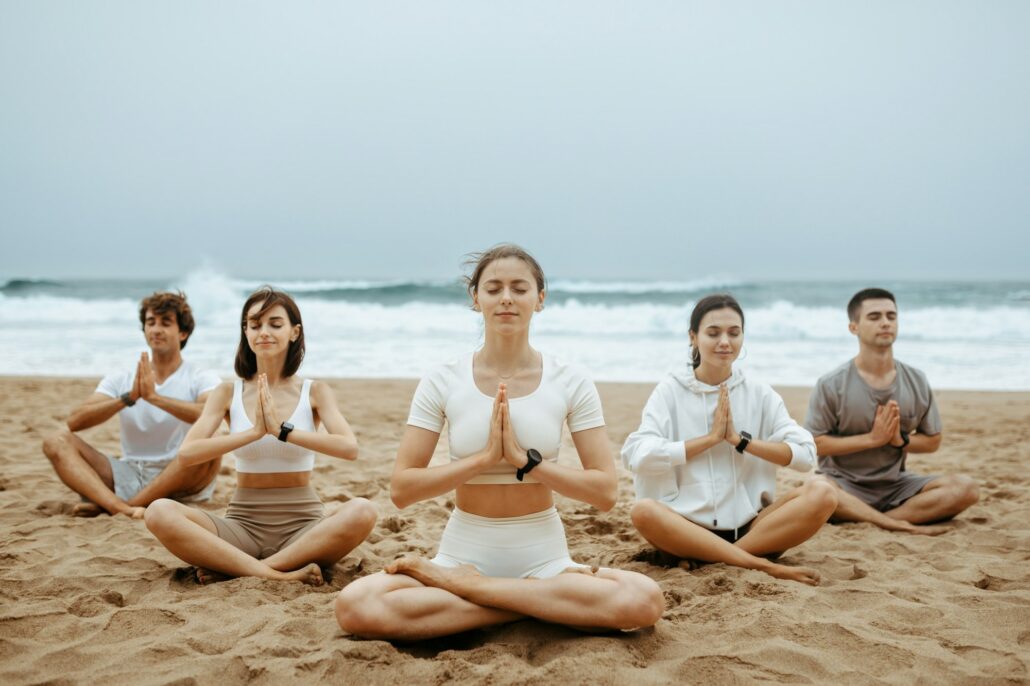 Beach meditation. Women and men practising yoga on beach, zen friends sitting in lotus position at